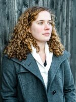 Portrait shot of Tabitha Mueller. She is standing against a wooden fence and looking away from the camera.