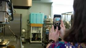 A woman holds a phone up taking apicture of a big blue tank inside a room
