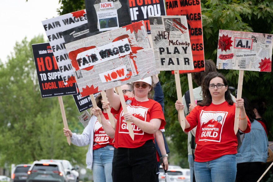 Men and women wearing red shirts hold signs on a street corner.