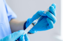 A health practictioner, mostly off-camera, fills a syringe with clear liquid.