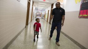 Torren Cooper, a Leading Men Fellow, walks with Kree Reid, 3, to a spot in the hallway of Turner Elementary School where they will work on literacy skills. (Tyrone Turner / WAMU)