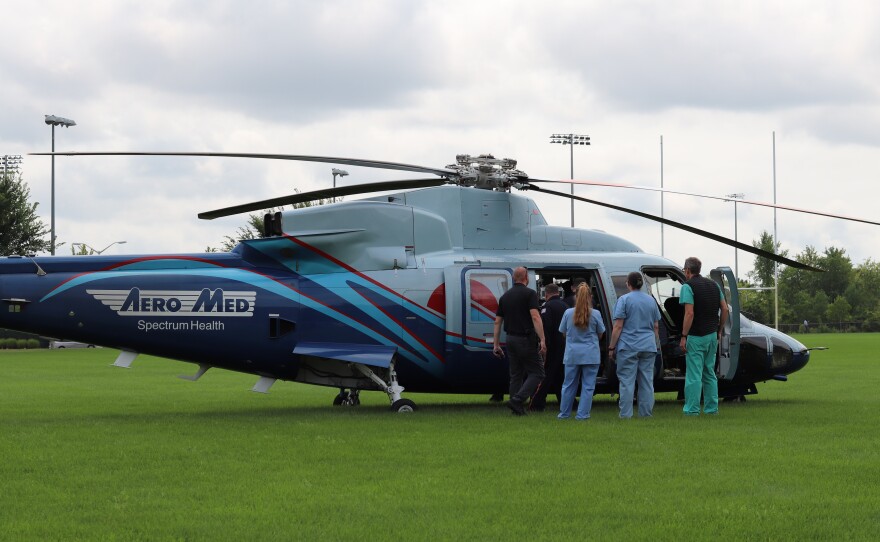 Four people wearing light blue scrubs and black clothes wait outside an open door of a helicopter.