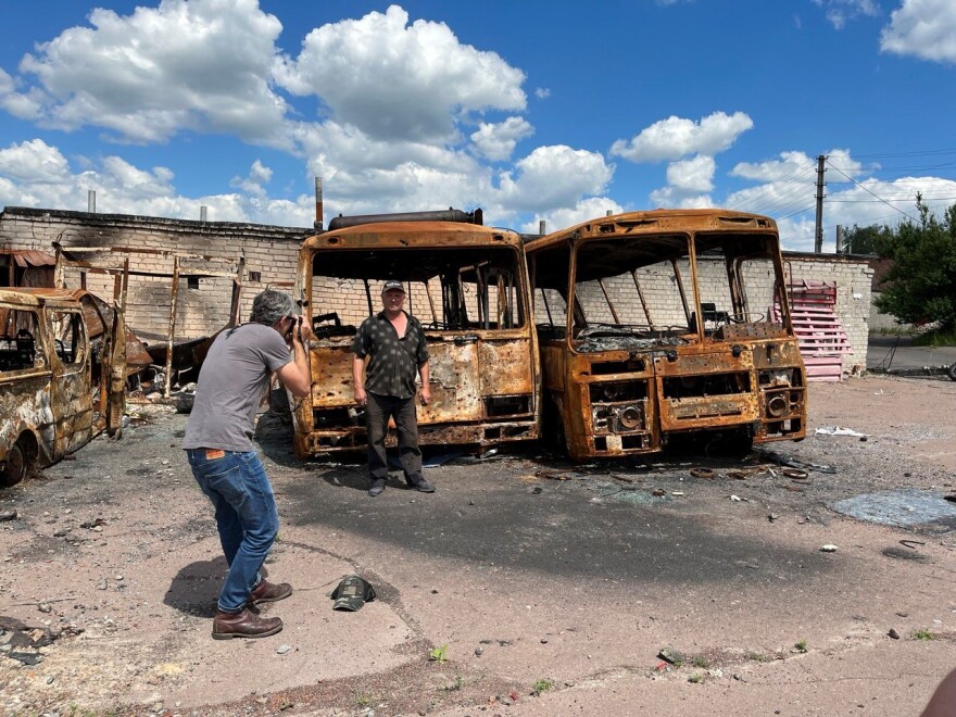 Patrick Patterson takes a photo of a man in front of two burnt out buses.