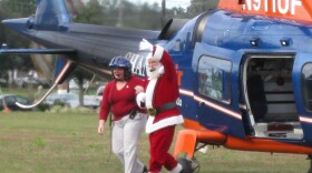 Santa Claus and a helper disembark from a helicopter during Operation Santa Delivery.