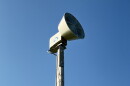 a siren on top of a light pole with blue sky behind it