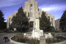 A strange white stone fountain with metal streamers instead of water sits outside a regal faded white stone building with the word courthouse etched above the front door