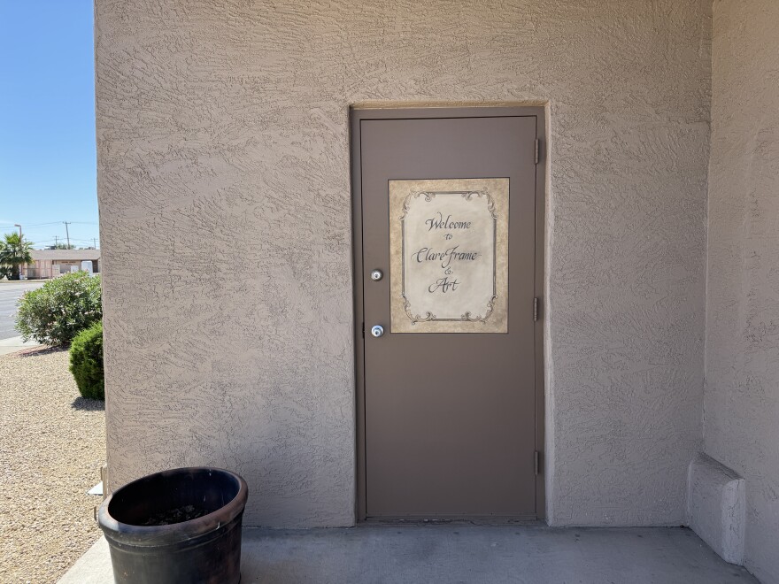 Dark brown door reads "Clare Framing and Art" in cursive on beige stucco walls