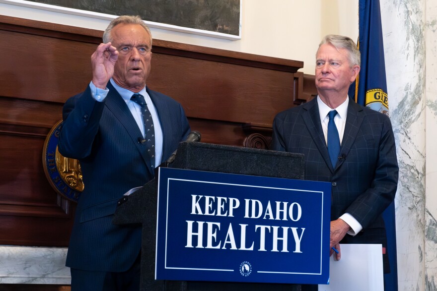 Two men in suits gather around a podium in front of a ceremonial fireplace.