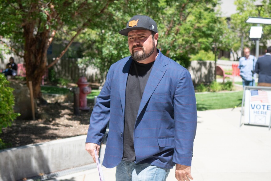 Robert Beadles looks at the camera while mid-stride. He wears a baseball cap and sport coat.