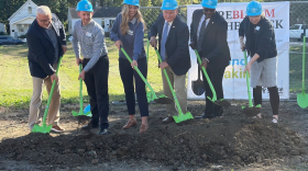 Six people holding green shovels break ground at a construction site