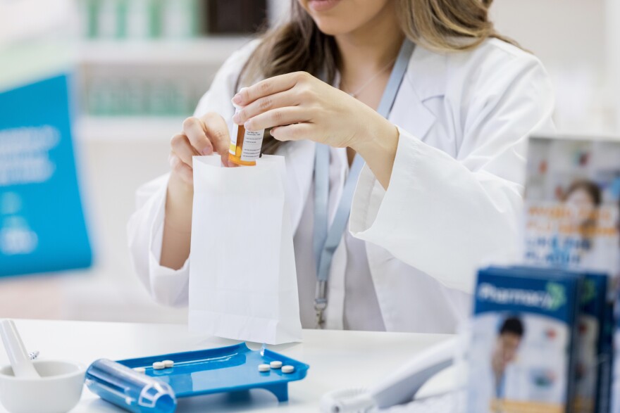 A pharmacist puts an orange prescription bottle in a white bag.