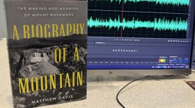 The cover of the book "A Biography of a Mountain" shows a black-and-white aerial image of Mount Rushmore National Memorial