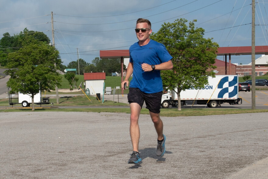 U.S. Air Force Capt. Alex Klinner wears a blue shirt and black shorts as he jogs along a road.