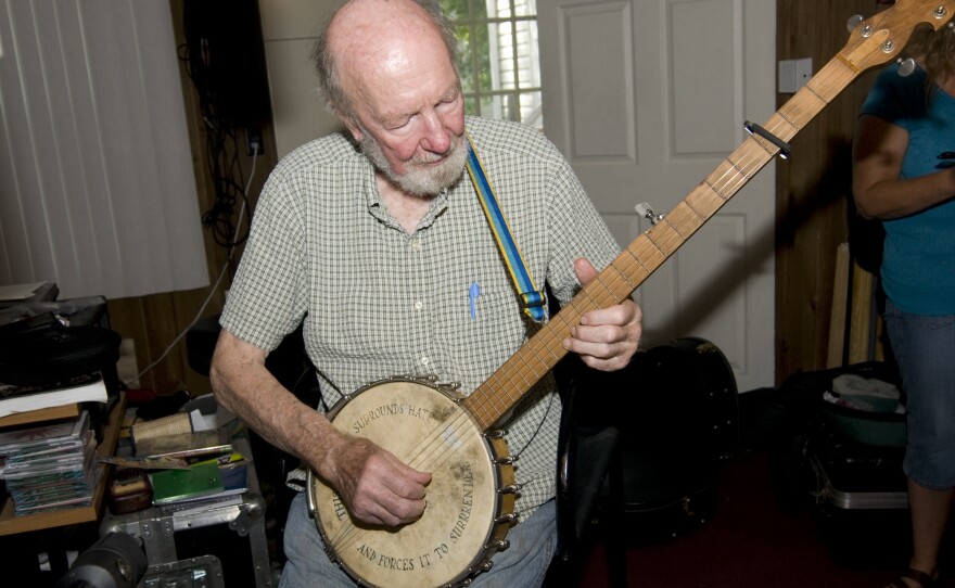 Seeger shows off his banjo, inscribed with the message, "This machine surrounds hate and forces it to surrender."