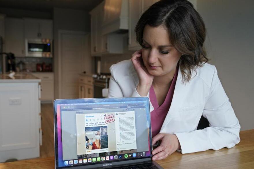 A woman dressed in a doctor's coat sits at her table and has her computer open to an Instagram post.