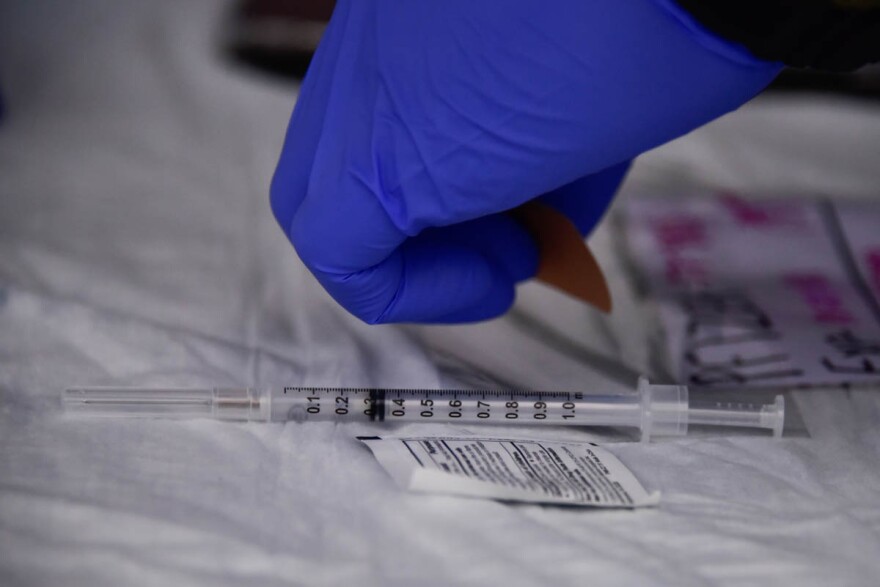  A hand in a blue glove reaches for a syringe next to a antibacterial wipe