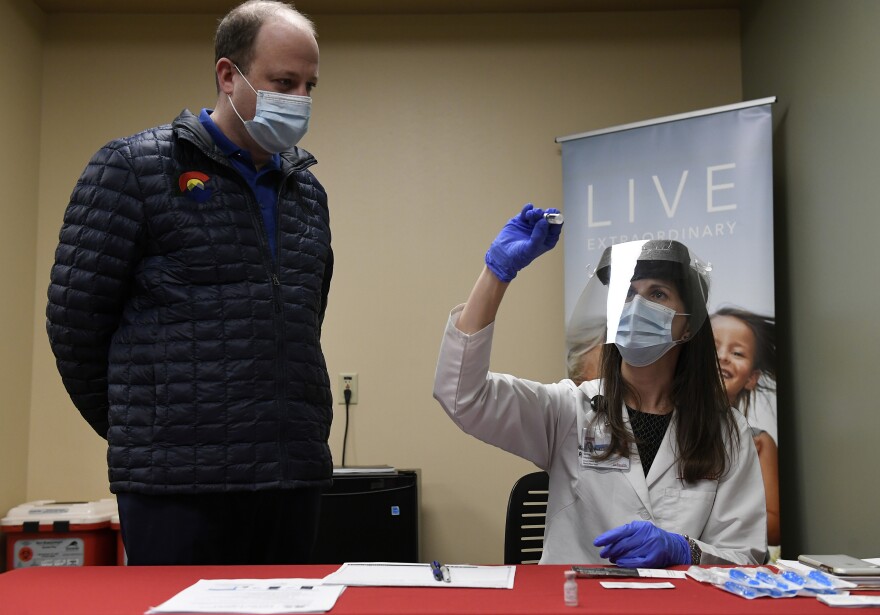 Gov. Jared Polis, left, watches as Gina Harper, clinical coordinator with pharmacy, right, reconstitutes a dose of the COVID-19 vaccine before it is administered to the first patients in Colorado at UC Health Poudre Valley Hospital on Dec. 14, 2020. During the process of preparing the vaccines, Harper adds sodium chloride to reconstitute the vaccine before injecting it into patients.