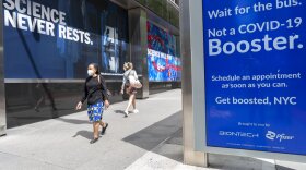 Pedestrians walk past a signs hanging outside Pfizer headquarters in New York and one hanging at a bus stop encouraging the Covid-19 booster, Monday, May 23, 2022.  