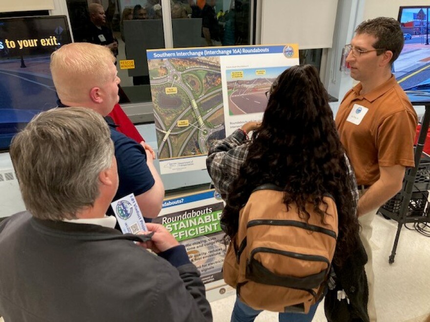 Four people gather to look at a rendering of a highway and surrounding roads.