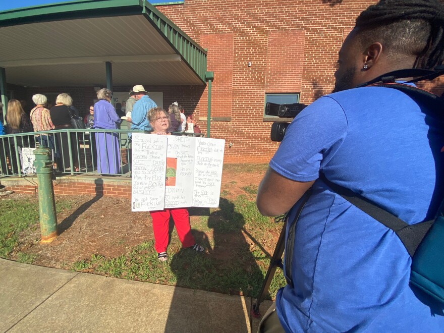 Diana Jimison tries to get her hand-lettered sign, filled with all the profanities she found in "Monday's Not Coming," into a TV interview before Monday's school board meeting.