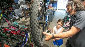 Cameron Berg, 7, helps Norte Chief Bike Mechanic Tyler Wituszynski inflate the tires on a bicycle she and her mother Beth Alexander of Washington, D.C., pick up for lessons on Wednesday from the Norte Wheelhouse Bike Library in Traverse City.