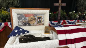 Casket with photos of Sgt. Adolph Aguirre and his uniform. American flag draped over. 