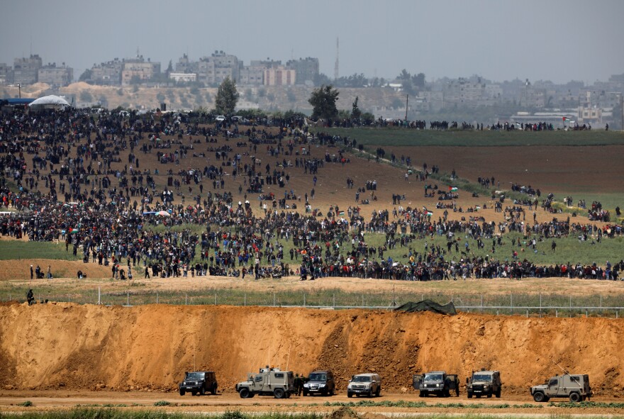 Israeli military vehicles are seen next to the border on the Israeli side of the Israel-Gaza border, as Palestinians demonstrate on the Gaza side of the border on Friday.