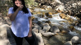 Olivia Carboni is standing next to a creek and looking at the camera and smiling.