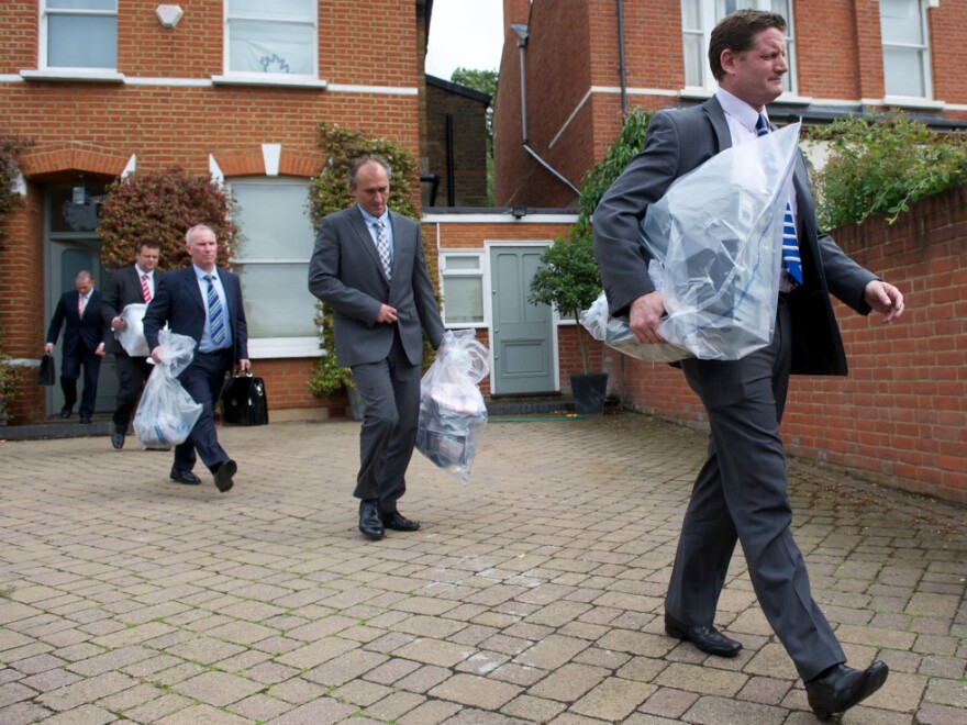 Investigators carry bags of evidence from the home of Andy Coulson, a former <em>News of the World</em> editor and Cameron aide, in London on Friday. Police arrested Coulson in the phone hacking scandal.