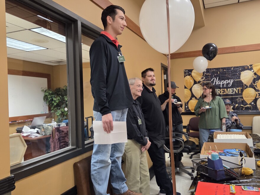 Lueken's Village Foods South Store Director Chris Washington stands on a chair as he prepares to give a speech celebrating Max Hites' career on May 1, 2026, who is standing on the right.