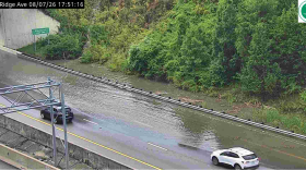 Floodwaters cover lanes of a highway as cars pass.