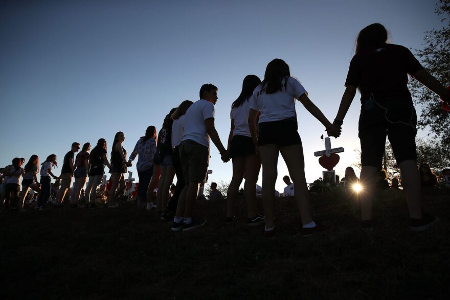Students and family members hold hands around a makeshift memorial in front of Marjory Stoneman Douglas High School in Parkland, Fla., where 17 people were killed on Feb. 14.