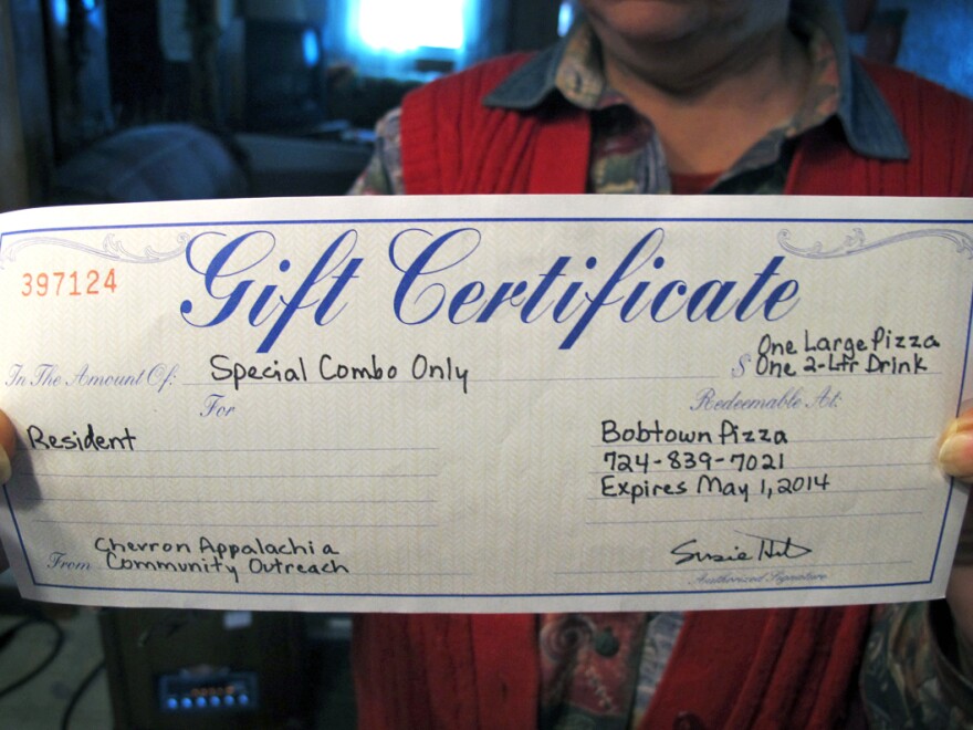 Joann Herrington holds up the gift certificate to Bobtown Pizza that she and her husband received from Chevron three days after a natural gas well exploded up the hill from their home in Mount Morris, Pa.