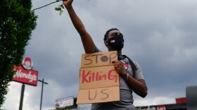 A man holds a sign and a white rose in his fist while facing traffic outside a burned Wendy's restaurant on the second day following the police shooting death of Rayshard Brooks in the restaurant parking lot June 14, 2020, in Atlanta, Georgia. (ELIJAH NOUVELAGE/AFP via Getty Images)