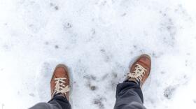 an image looking down at brown boots and grey pants standing on top of snow