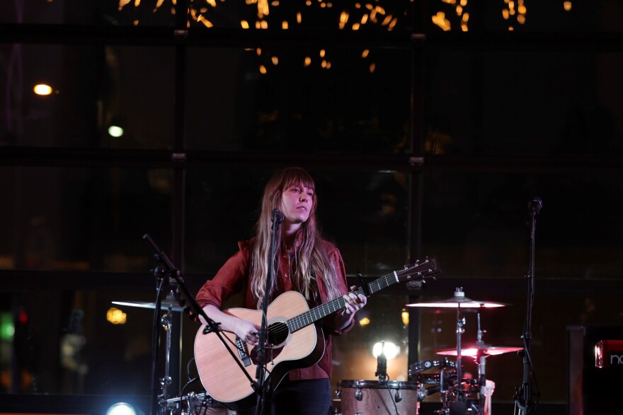 Musician Kelley Smith holding a guitar with a microphone in front of her.