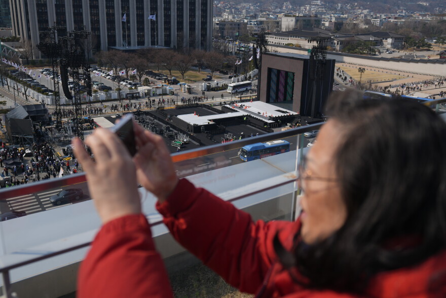 A woman films with her smartphone near a stage for a concert by K-pop group BTS at Gwanghwamun Square in Seoul, South Korea, Friday, March 20, 2026.