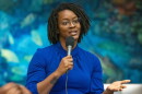 black woman in blue dress standing and talking into a microphone