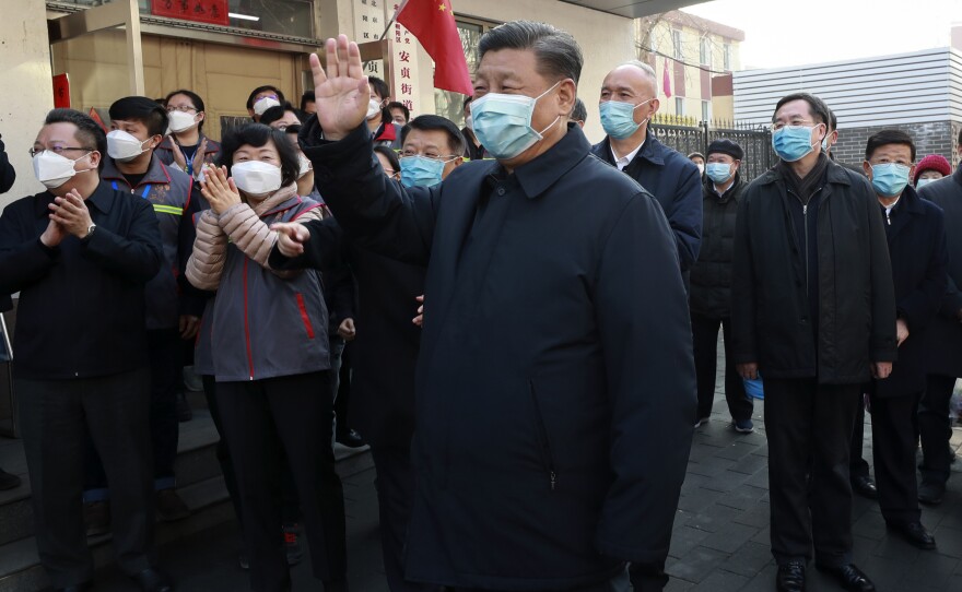 In this photo released by Xinhua News Agency, Chinese President Xi Jinping, center, wearing a protective face mask waves as he inspects the novel coronavirus pneumonia prevention and control work at a neighborhood in Beijing on Monday.