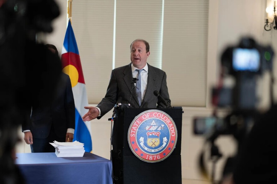 Colorado Gov. Jared Polis points to a copy of the so-called big, beautiful bill, the Republican federal tax and spending measure, as he speaks to reporters about his decision to call a special legislative session to address a nearly $1 billion budget deficit during a news conference at the governor’s mansion in downtown Denver on Wednesday, Aug. 6, 2025.