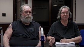 A man and a woman wearing black shirts, holding paperwork and a walker