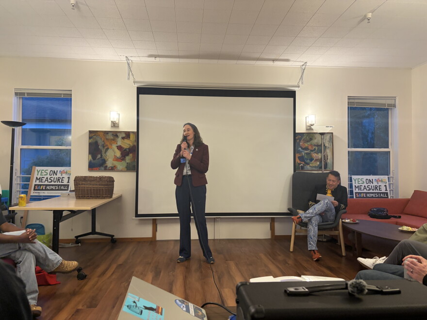  Mayor Katie Wilson speaks to a room next to signs that say "Yes on measure 1." 