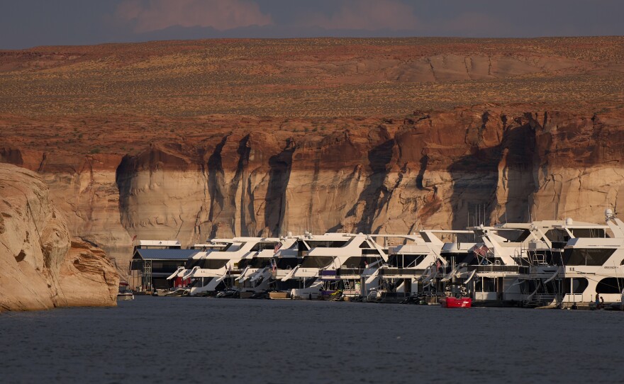 Houseboats are moored at the Antelope Point Marina on Lake Powell at the Glen Canyon National Recreation Area, Wednesday, July 15, 2026, near Page, Ariz. A bathtub ring of light minerals on the canyon walls show the high water mark of the reservoir. (AP Photo/John Locher)