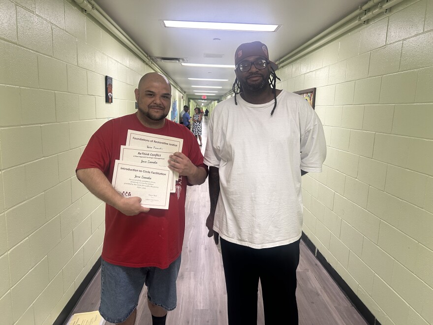 TCKC resident Jose and Doyle seen together in hallway with Jose showing off his certificates. 