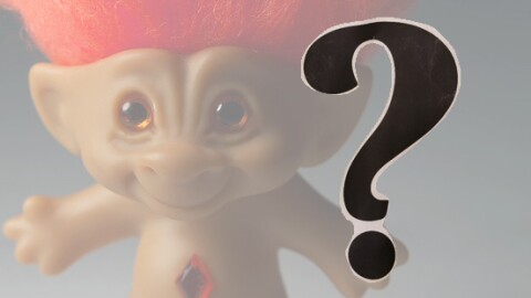 A troll doll with orange hair, a black question mark in the foreground
