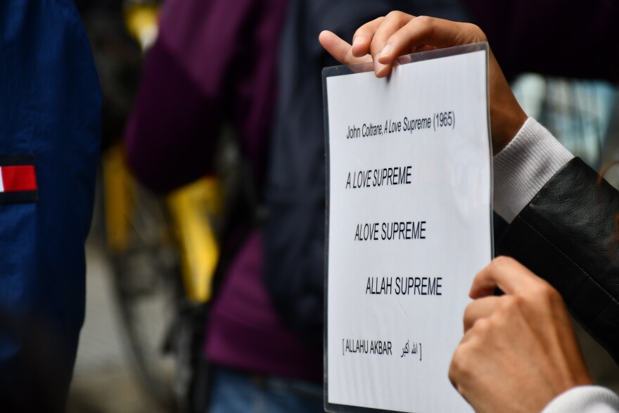 A tour participant holds up the lyrics of John Coltrane's <em>A Love Supreme </em>outside the Apollo Theater as guide Katie Merriman speaks about the song's interpretation as a Sufi Muslim prayer.