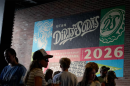 A colorful mural on a brick wall reads "Utah Dirty Sodas" and "2026." A crowd of people stand in front of it, facing different directions. 