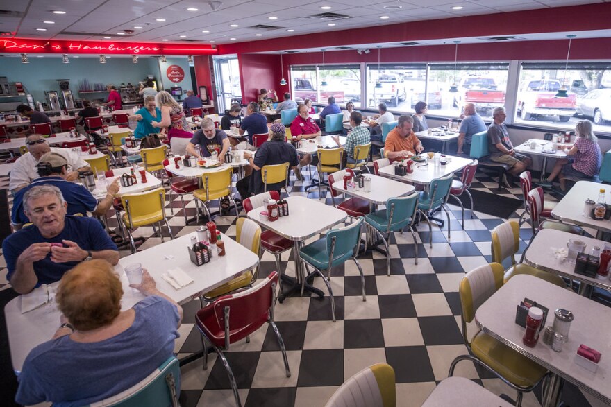  The inside of a Dan's Hamburgers. There is a very retro look, complete with checkered floors and plastic, colorful chairs. 