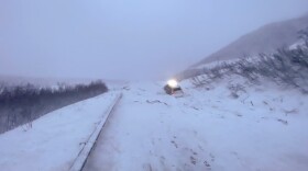 A van sits half-buried in avalanche debris on a rural highway.