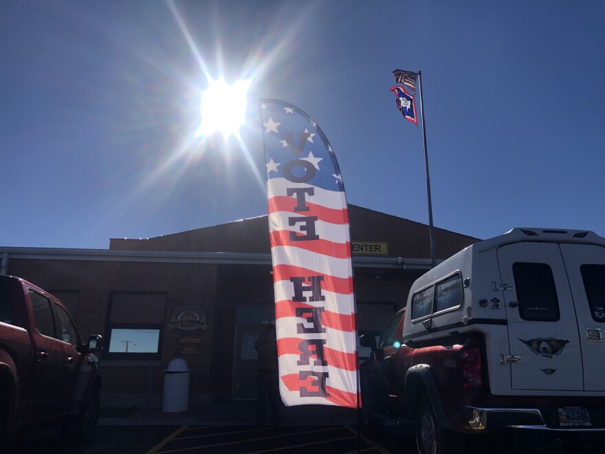 A sign reads "vote here" outside of a building with a few trucks parked near it